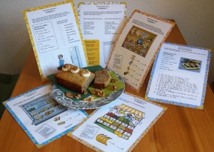 Bunte Arbeitsblätter zu Bibelkuchen oder Bananenkuchen, ausgedruckt und angeordnet auf einem Tisch, mit einem Kuchen in der Mitte.